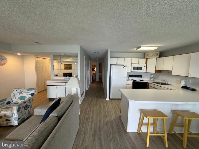 kitchen featuring a kitchen breakfast bar, kitchen peninsula, wood-type flooring, a textured ceiling, and white appliances