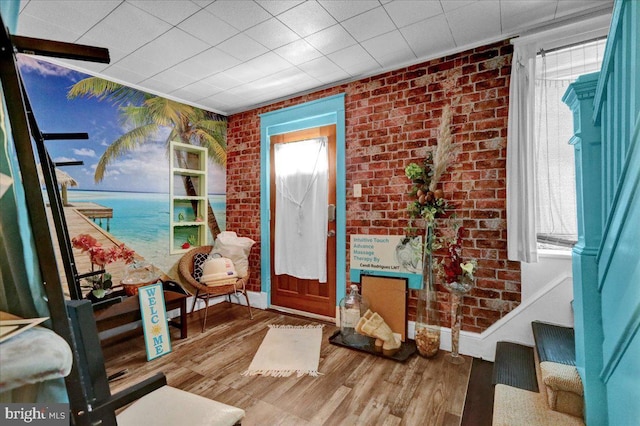 entryway with a water view, a healthy amount of sunlight, brick wall, and hardwood / wood-style flooring