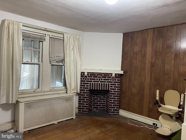 unfurnished living room featuring wooden walls, dark hardwood / wood-style floors, radiator, and a brick fireplace