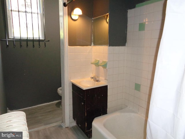 full bathroom featuring shower / bath combo, vanity, tile walls, hardwood / wood-style floors, and toilet