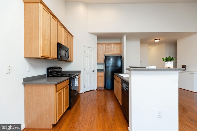 kitchen with light brown cabinetry, light hardwood / wood-style flooring, black appliances, and a high ceiling