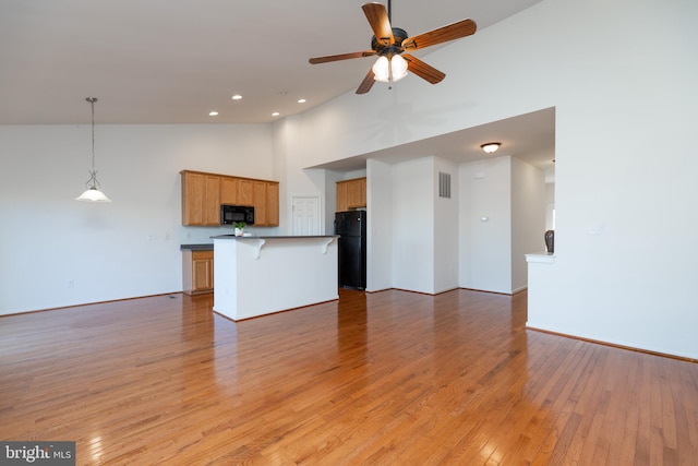 kitchen featuring a center island, high vaulted ceiling, decorative light fixtures, black appliances, and light wood-type flooring