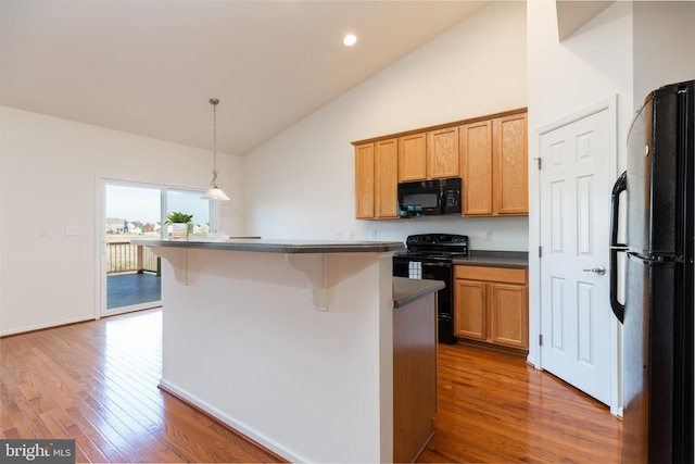 kitchen featuring dark wood-type flooring, black appliances, decorative light fixtures, a kitchen island, and a kitchen bar