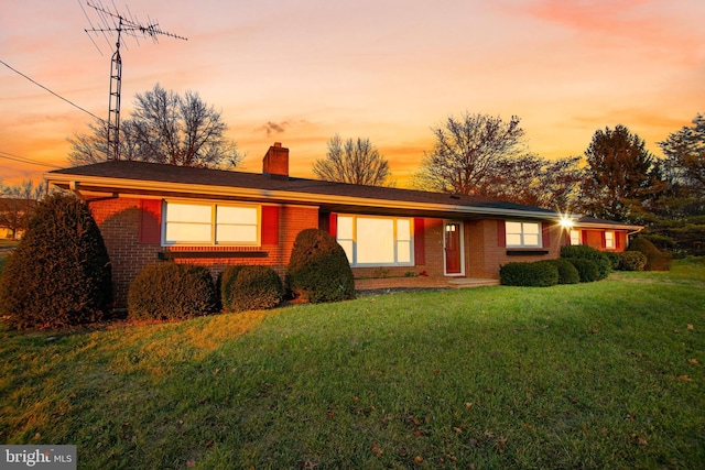 view of front of home featuring brick siding, a lawn, and a chimney