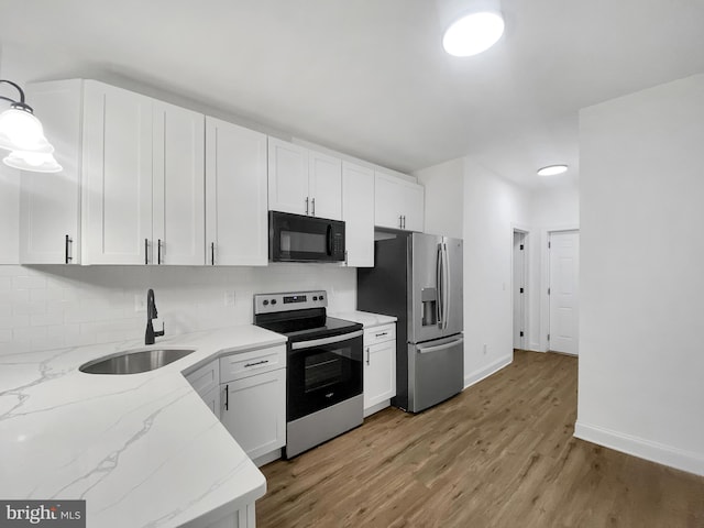 kitchen featuring appliances with stainless steel finishes, light wood-type flooring, sink, white cabinetry, and hanging light fixtures