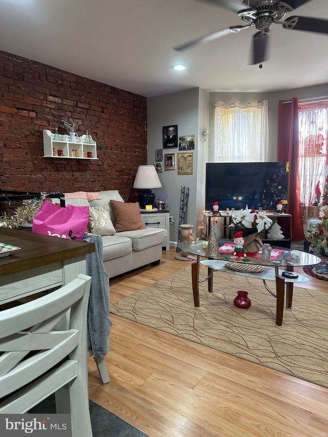 living room featuring hardwood / wood-style floors, ceiling fan, and brick wall