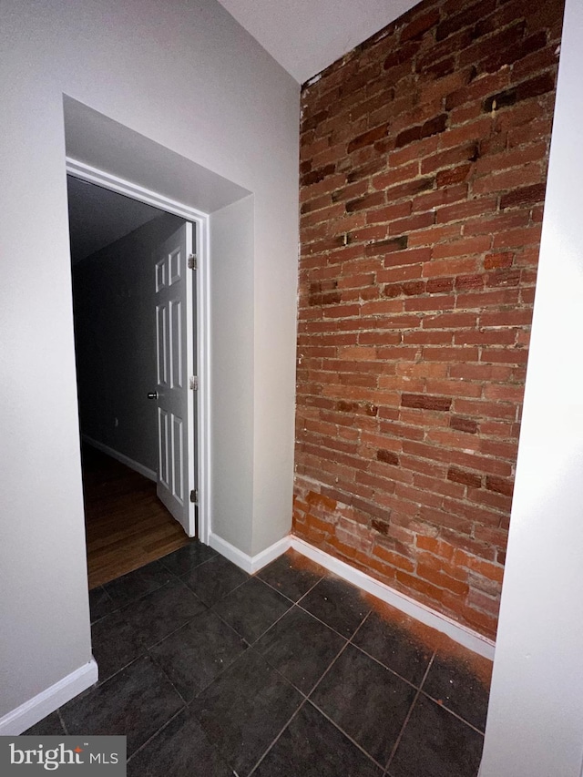 spare room with dark tile patterned floors and brick wall