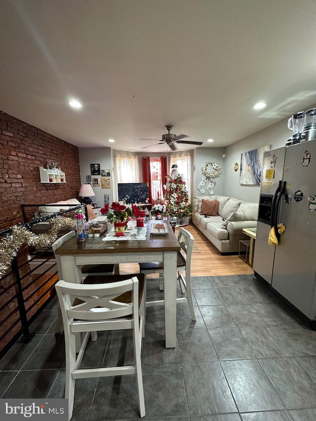 dining area featuring ceiling fan, wood-type flooring, and brick wall