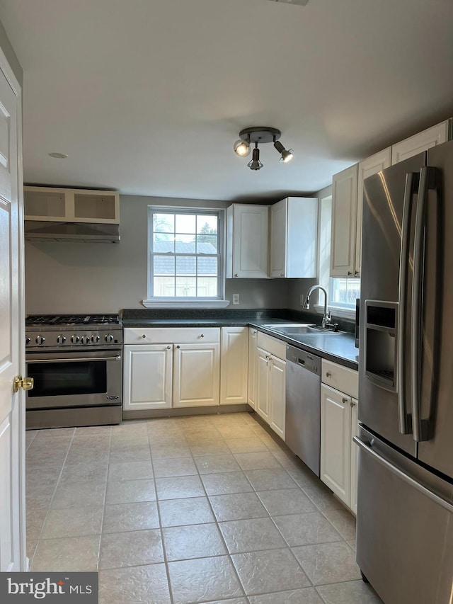 kitchen with sink, light tile patterned flooring, range hood, white cabinets, and appliances with stainless steel finishes