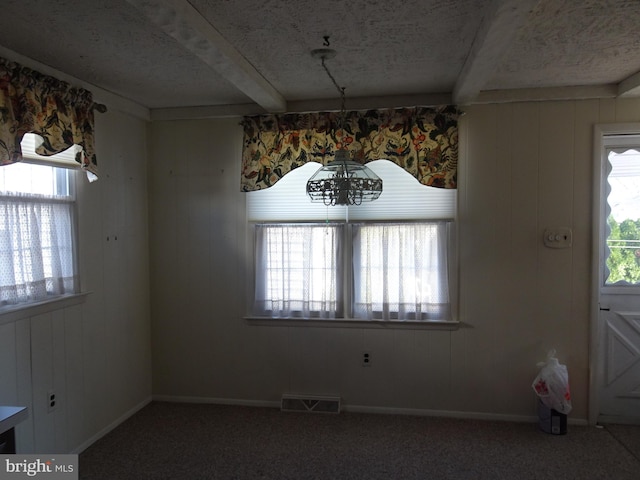 unfurnished dining area featuring carpet, plenty of natural light, beam ceiling, and an inviting chandelier