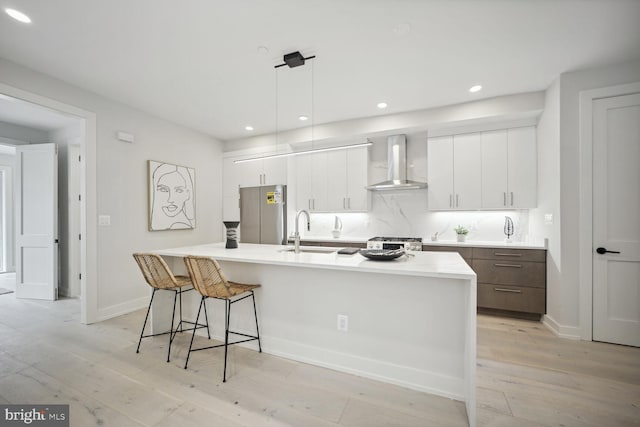 kitchen with sink, stainless steel appliances, wall chimney range hood, a kitchen island with sink, and white cabinets