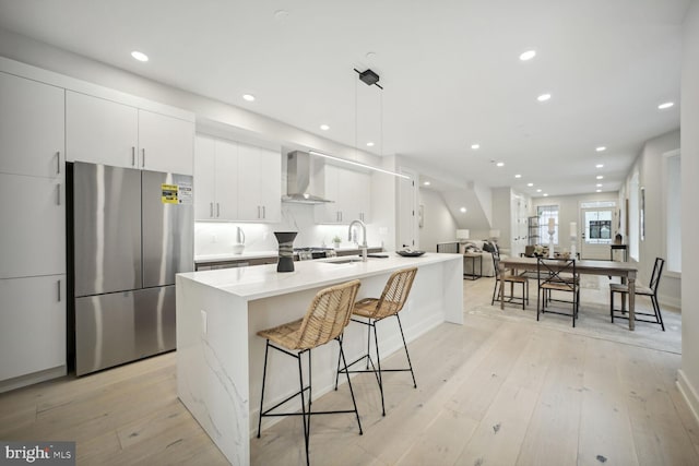 kitchen featuring wall chimney exhaust hood, stainless steel fridge, light wood-type flooring, and white cabinetry