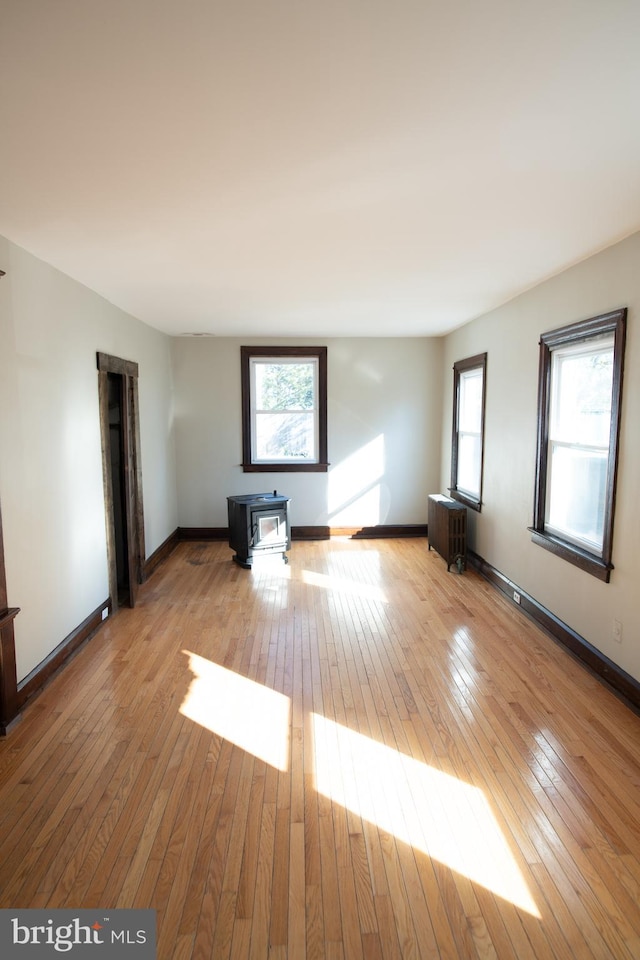 spare room with radiator heating unit, light hardwood / wood-style floors, and a wood stove