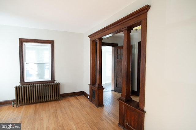 unfurnished room featuring light hardwood / wood-style floors, radiator, and decorative columns