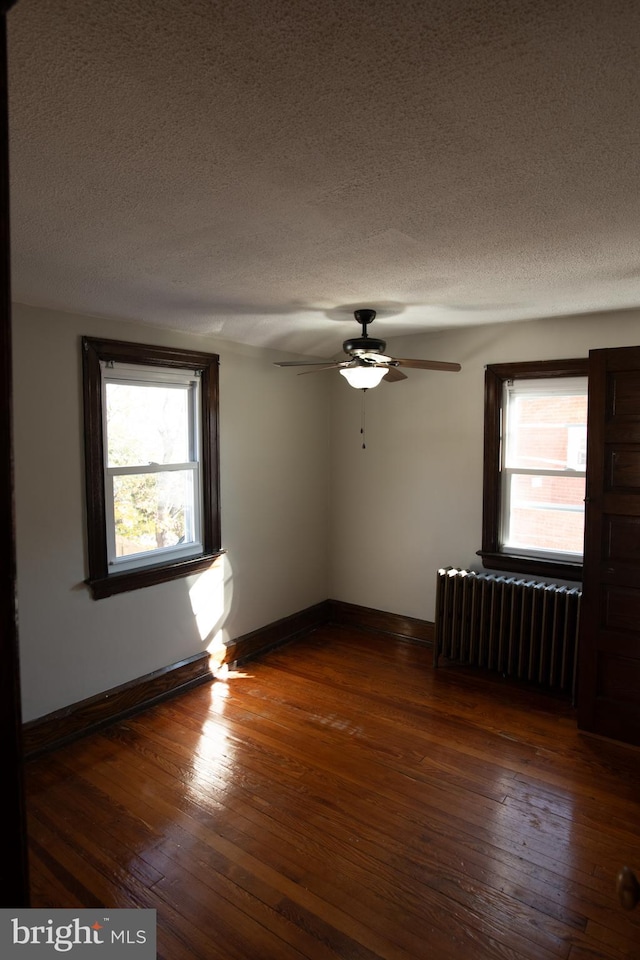 empty room featuring a wealth of natural light, dark wood-type flooring, and radiator