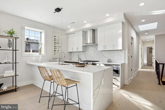 kitchen featuring pendant lighting, wall chimney range hood, sink, light hardwood / wood-style flooring, and a skylight