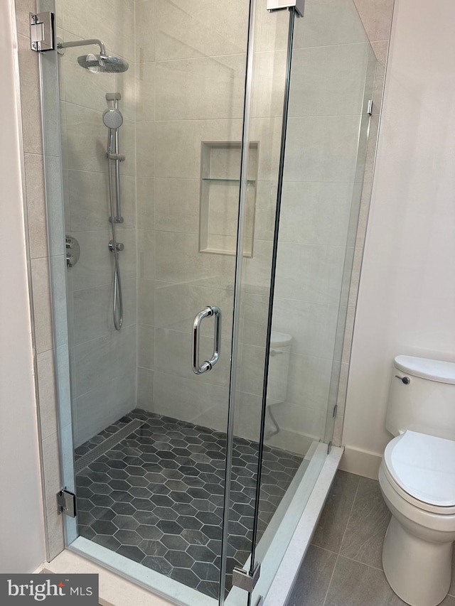 bathroom featuring tile patterned flooring, toilet, and a shower with shower door