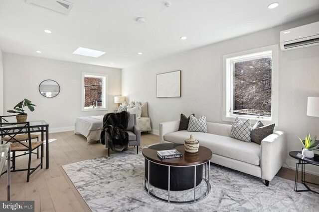 living room with light hardwood / wood-style floors, an AC wall unit, and a skylight