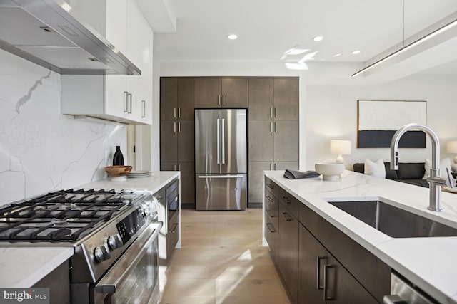 kitchen with appliances with stainless steel finishes, backsplash, sink, wall chimney range hood, and white cabinets