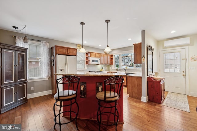 kitchen with a wall mounted air conditioner, dark hardwood / wood-style flooring, white appliances, decorative light fixtures, and a kitchen island