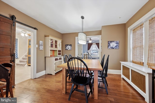 dining space with a barn door, ceiling fan, and light hardwood / wood-style floors