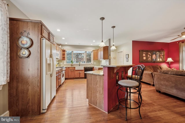 kitchen featuring a kitchen bar, sink, black dishwasher, light hardwood / wood-style floors, and white fridge with ice dispenser