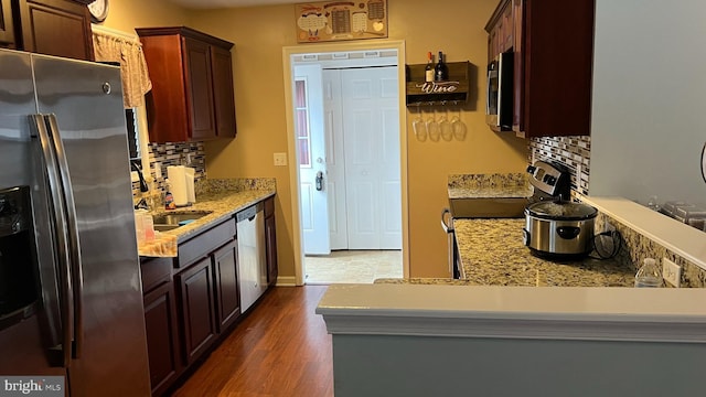 kitchen with dark hardwood / wood-style floors, kitchen peninsula, stainless steel appliances, and tasteful backsplash