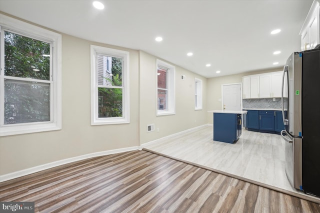 kitchen with white cabinets, blue cabinets, a kitchen island, a breakfast bar area, and stainless steel refrigerator