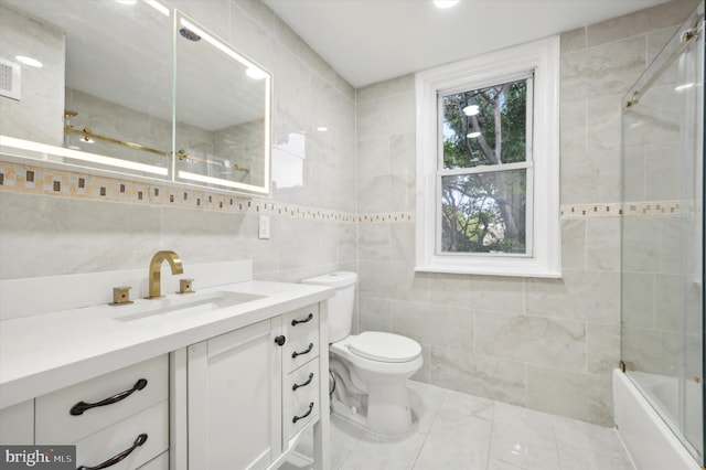 full bathroom featuring vanity, toilet, bath / shower combo with glass door, and tile walls