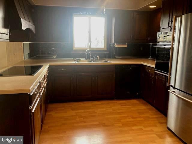 kitchen featuring decorative backsplash, light wood-type flooring, dark brown cabinets, sink, and black appliances