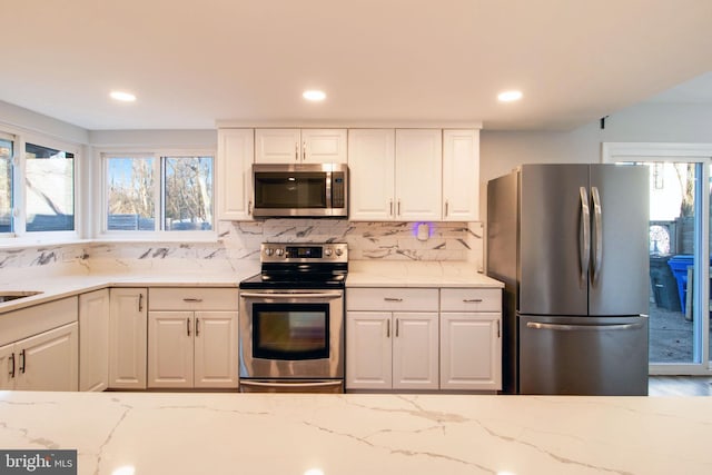 kitchen featuring white cabinets, decorative backsplash, light stone countertops, and stainless steel appliances