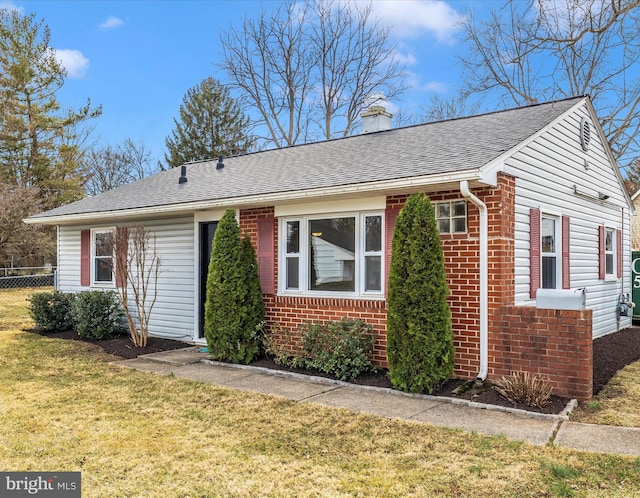 view of front of home featuring a front yard, brick siding, a chimney, and roof with shingles