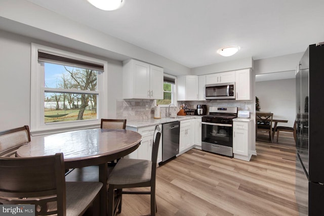 kitchen featuring white cabinets, sink, light hardwood / wood-style flooring, decorative backsplash, and stainless steel appliances