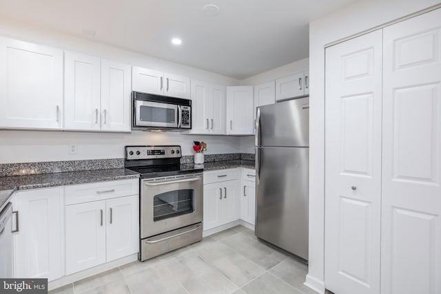 kitchen featuring dark stone countertops, white cabinetry, light tile patterned floors, and appliances with stainless steel finishes