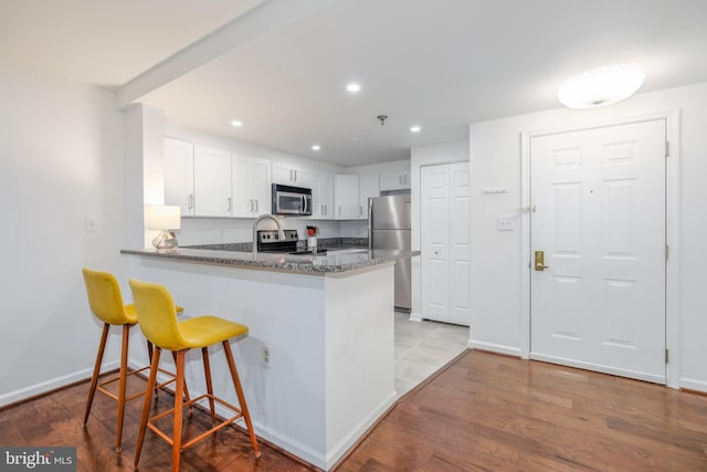 kitchen with dark stone counters, kitchen peninsula, light hardwood / wood-style flooring, appliances with stainless steel finishes, and white cabinetry