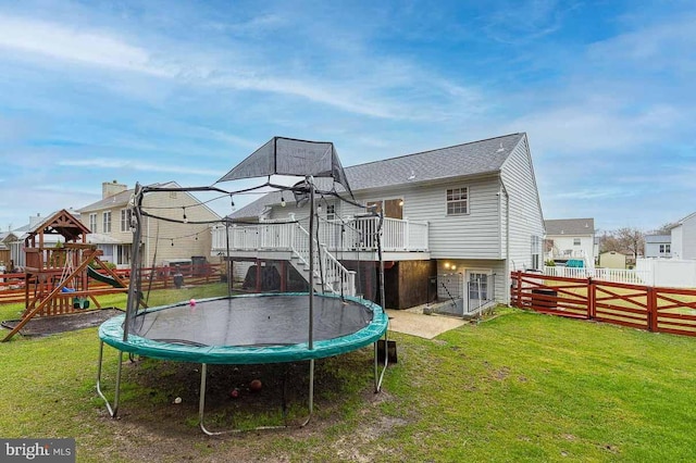 rear view of house featuring a playground, a yard, a trampoline, and a wooden deck