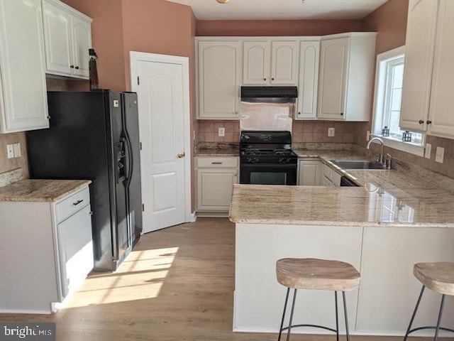 kitchen with sink, white cabinetry, a kitchen breakfast bar, kitchen peninsula, and black appliances