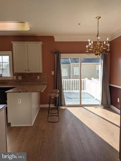 kitchen with crown molding, hanging light fixtures, hardwood / wood-style floors, backsplash, and white cabinets