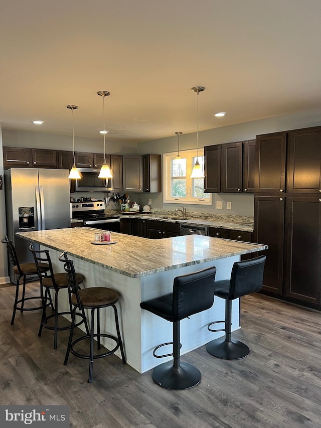 kitchen with a kitchen bar, stainless steel appliances, dark hardwood / wood-style floors, hanging light fixtures, and a large island