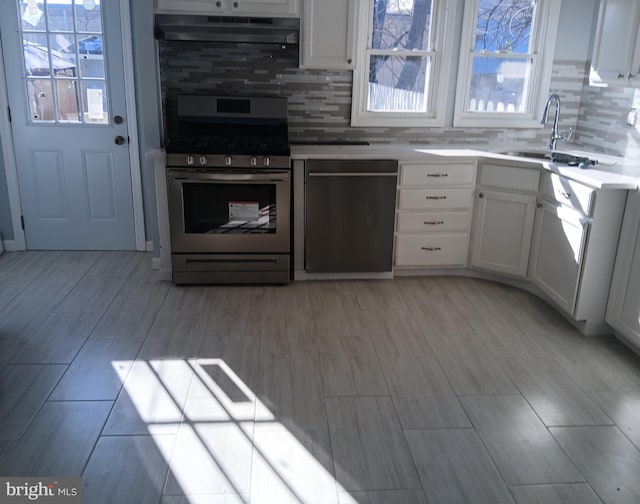 kitchen featuring stainless steel gas range, dishwashing machine, exhaust hood, sink, and white cabinetry