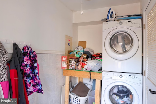 clothes washing area featuring stacked washer / dryer and tile walls