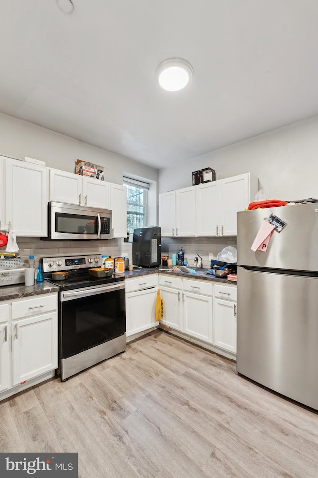 kitchen with white cabinets, appliances with stainless steel finishes, light hardwood / wood-style floors, and decorative backsplash