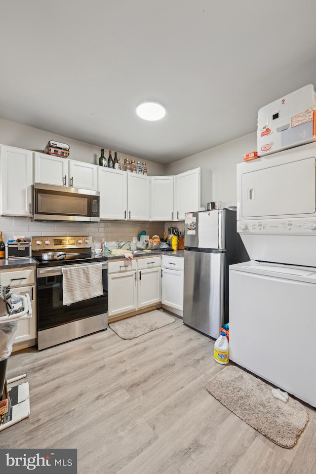 kitchen with white cabinetry, tasteful backsplash, stacked washer / drying machine, appliances with stainless steel finishes, and light wood-type flooring