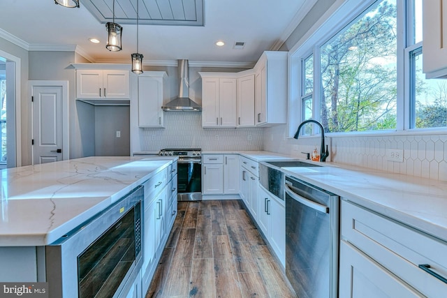 kitchen featuring white cabinetry, sink, stainless steel appliances, wall chimney range hood, and decorative light fixtures