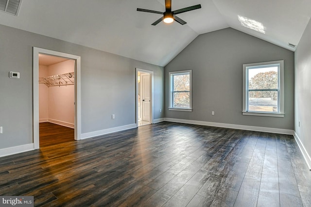 unfurnished bedroom with a walk in closet, ceiling fan, dark wood-type flooring, and multiple windows