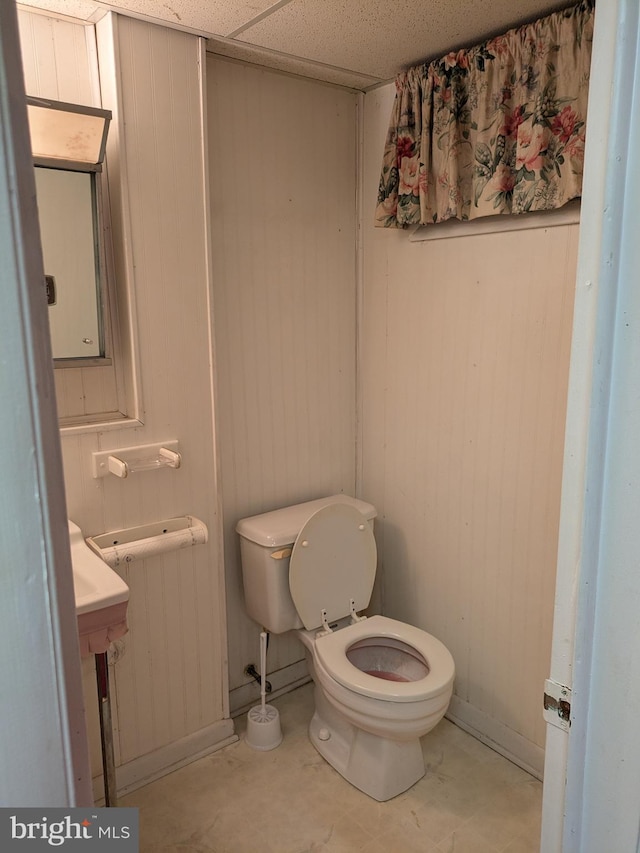 bathroom with radiator heating unit, toilet, a drop ceiling, and wood walls