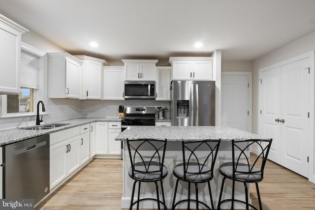 kitchen featuring sink, light wood-type flooring, appliances with stainless steel finishes, a kitchen island, and light stone counters