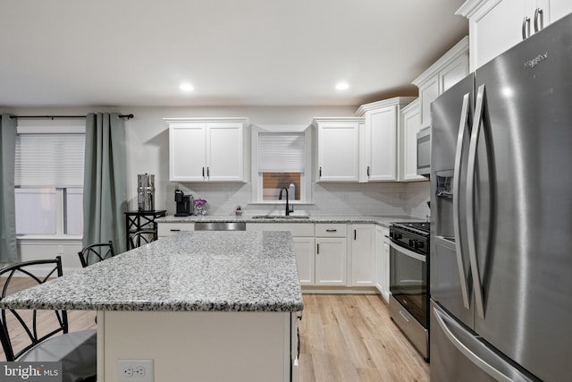 kitchen featuring a center island, appliances with stainless steel finishes, light stone counters, white cabinetry, and a breakfast bar area