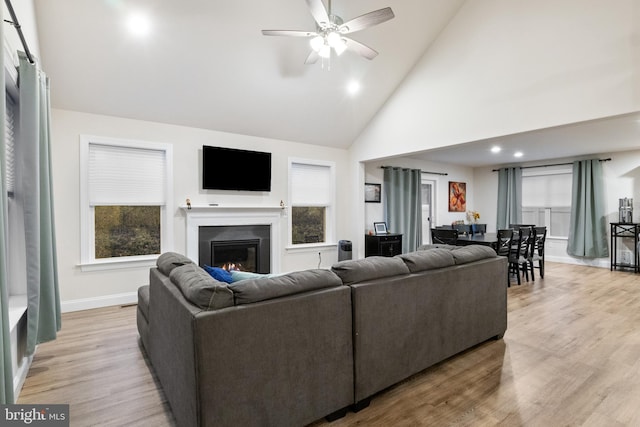 living room with a wealth of natural light, light hardwood / wood-style flooring, high vaulted ceiling, and ceiling fan