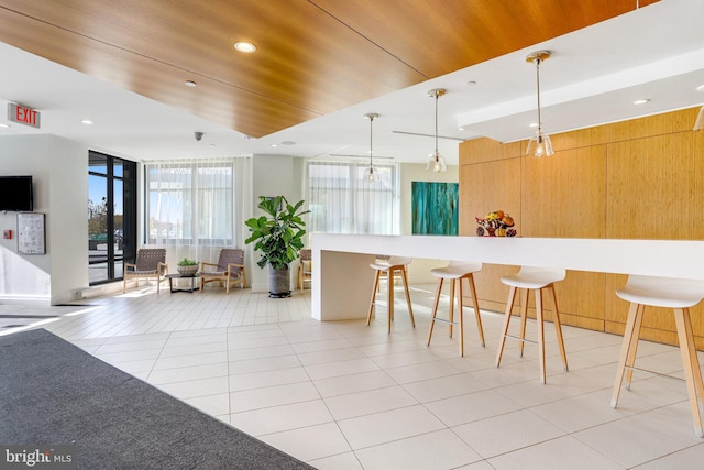 kitchen featuring pendant lighting, wooden ceiling, light tile patterned flooring, a kitchen bar, and a wall of windows